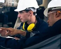Dois técnicos de capacete analisando um desenho técnico durante avaliação de peça industrial para cromo duro
